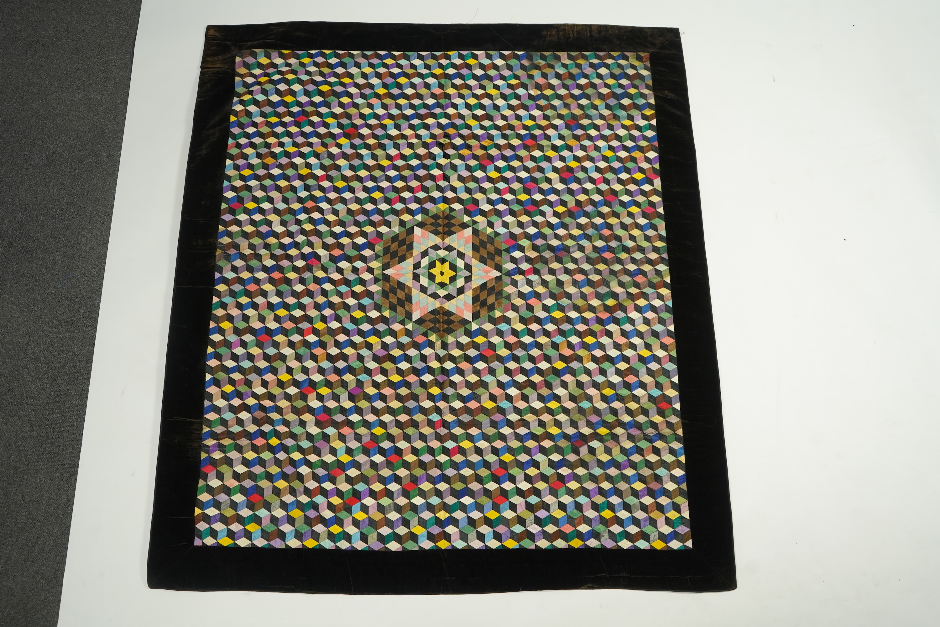 An English 19th century silk ‘Tumbling Blocks’, hand sewn, patchwork quilt, with central star motif and wide velvet border. Worked with multi coloured silks backed with black and blue silk., 170cm x 152cm. Condition - th
